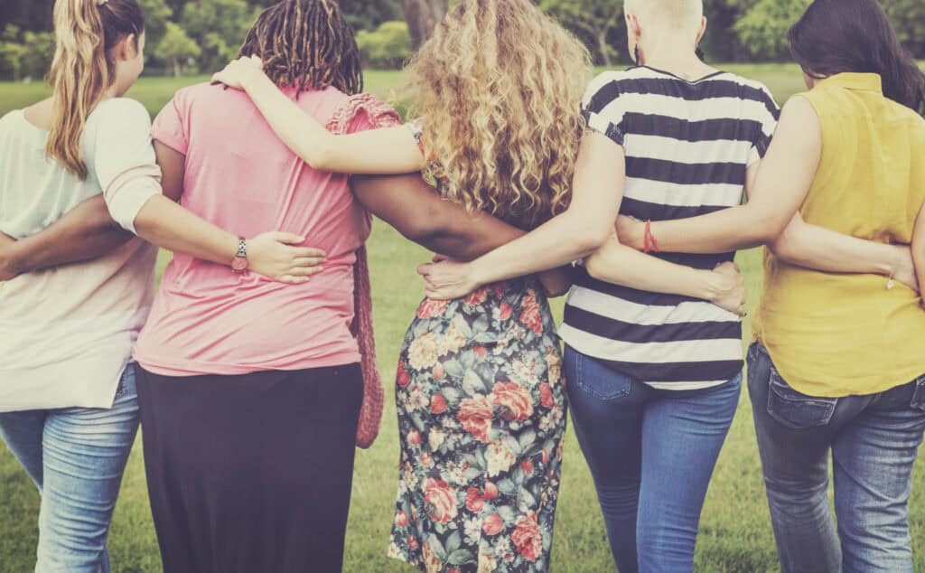 Group of diverse women standing together with arms around each other outdoors.
