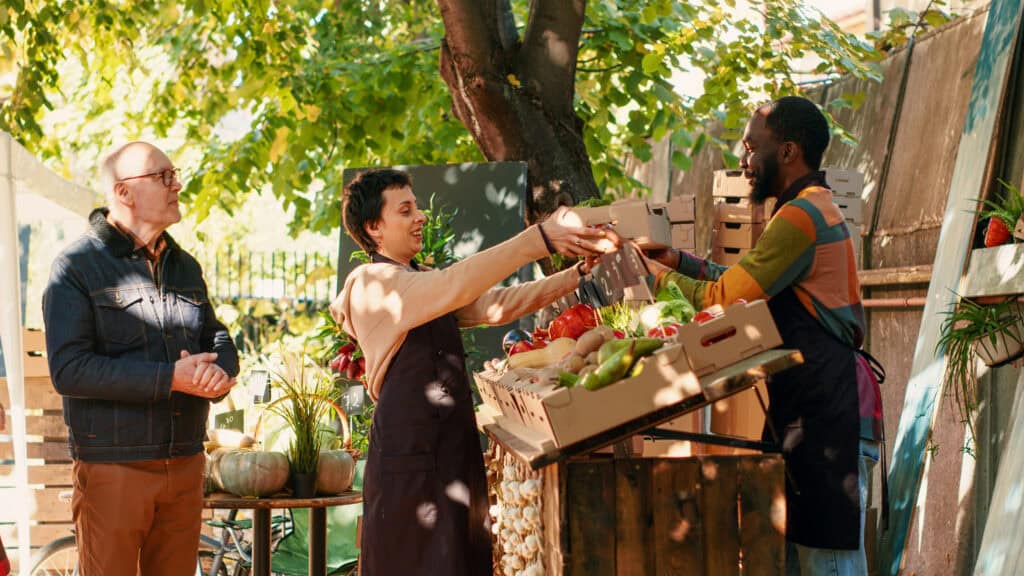 People exchanging goods at a community market stall outdoors.