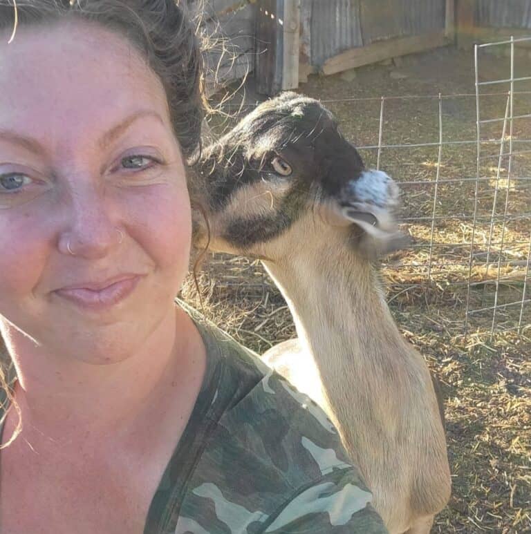 Woman with a goat on her shoulder in a farm setting.