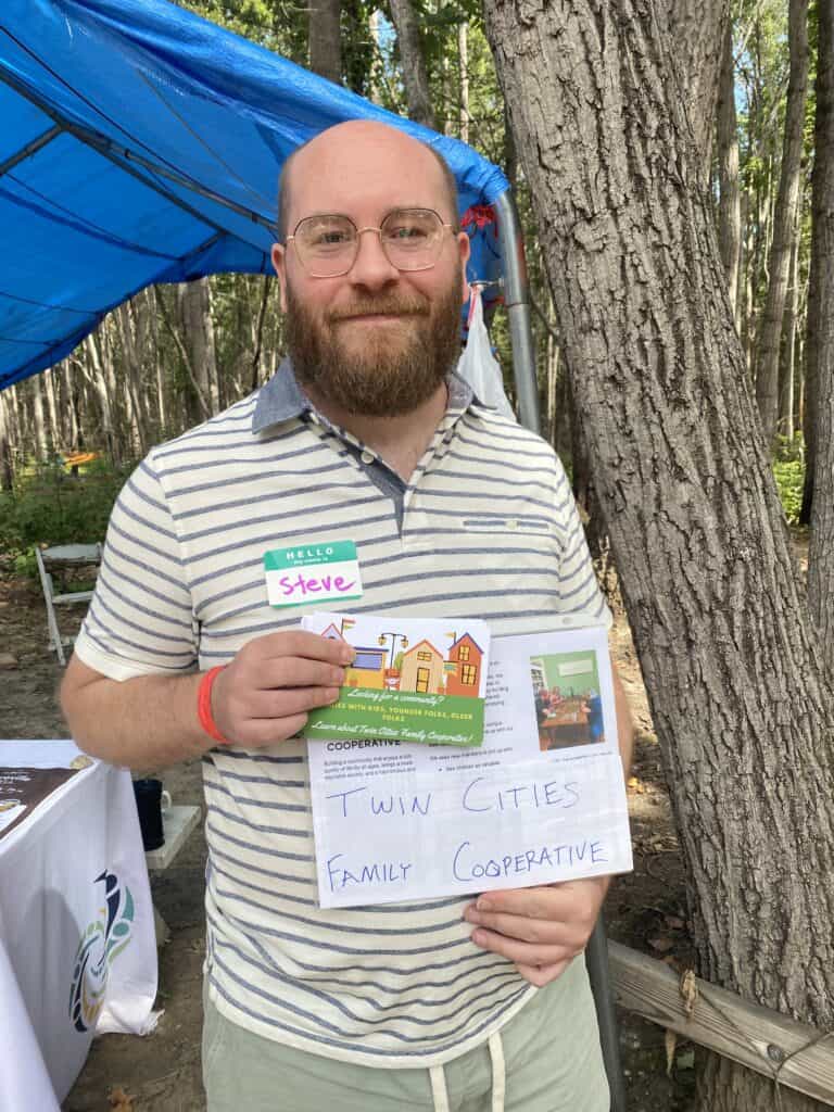 Man holding Twin Cities Family Cooperative sign at community event.