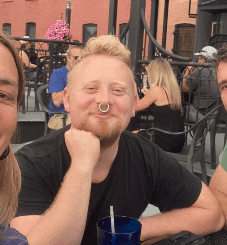 Smiling man with a septum piercing at an outdoor cafe during daytime.