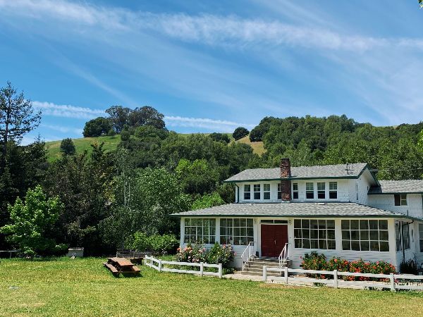 Scenic view of a white house with a porch in a lush green landscape.