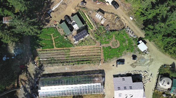 Aerial view of a forest garden with greenhouses, garden beds, and surrounding trees.