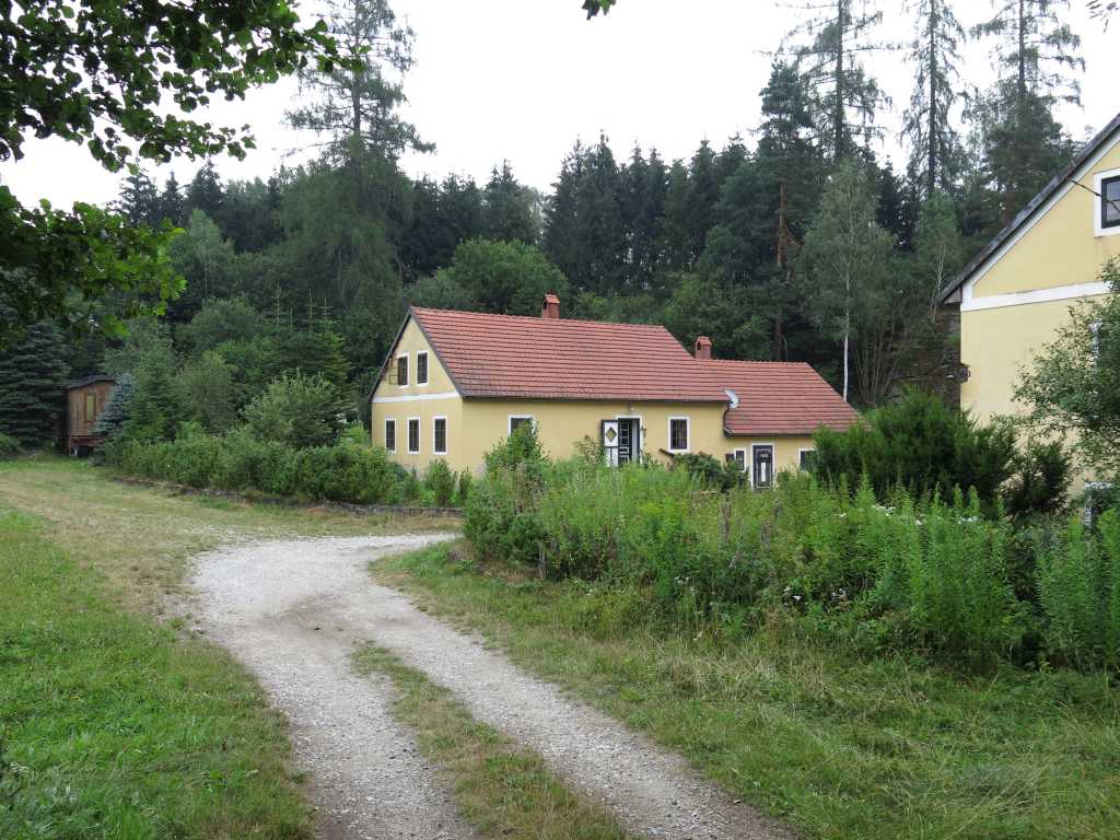 Cozy yellow house with red roof in a lush green rural setting.