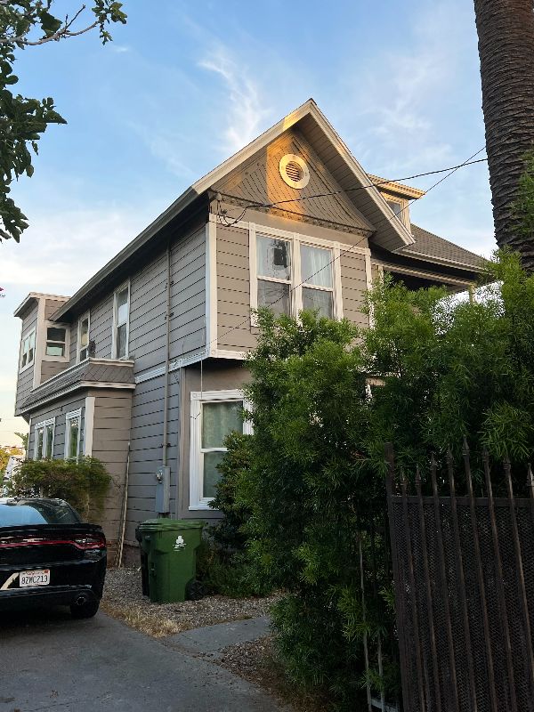 Victorian-style house with gray siding and lush greenery in front.