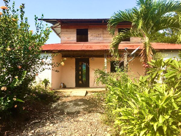 Rustic two-story house surrounded by lush tropical plants in Ecuador.