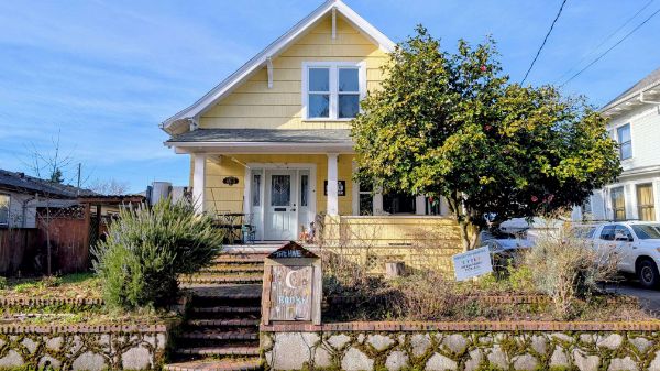 Yellow house with front porch and large tree in a community setting.