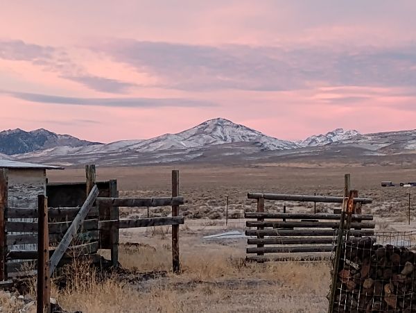 Scenic view of mountains and open land at sunset with rustic fencing.