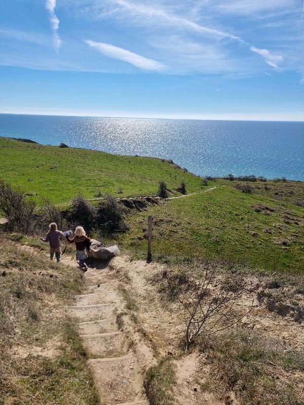 Two children walking down a coastal trail with ocean view and blue sky.