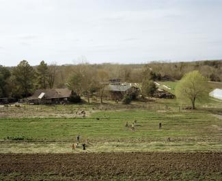 Rural community farm with people working in fields and trees in the background.