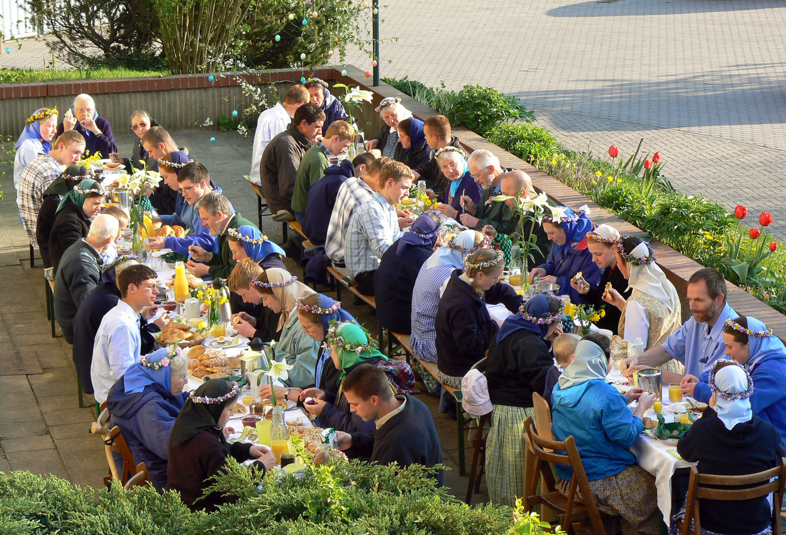 Community gathering with people enjoying outdoor meal at long tables.
