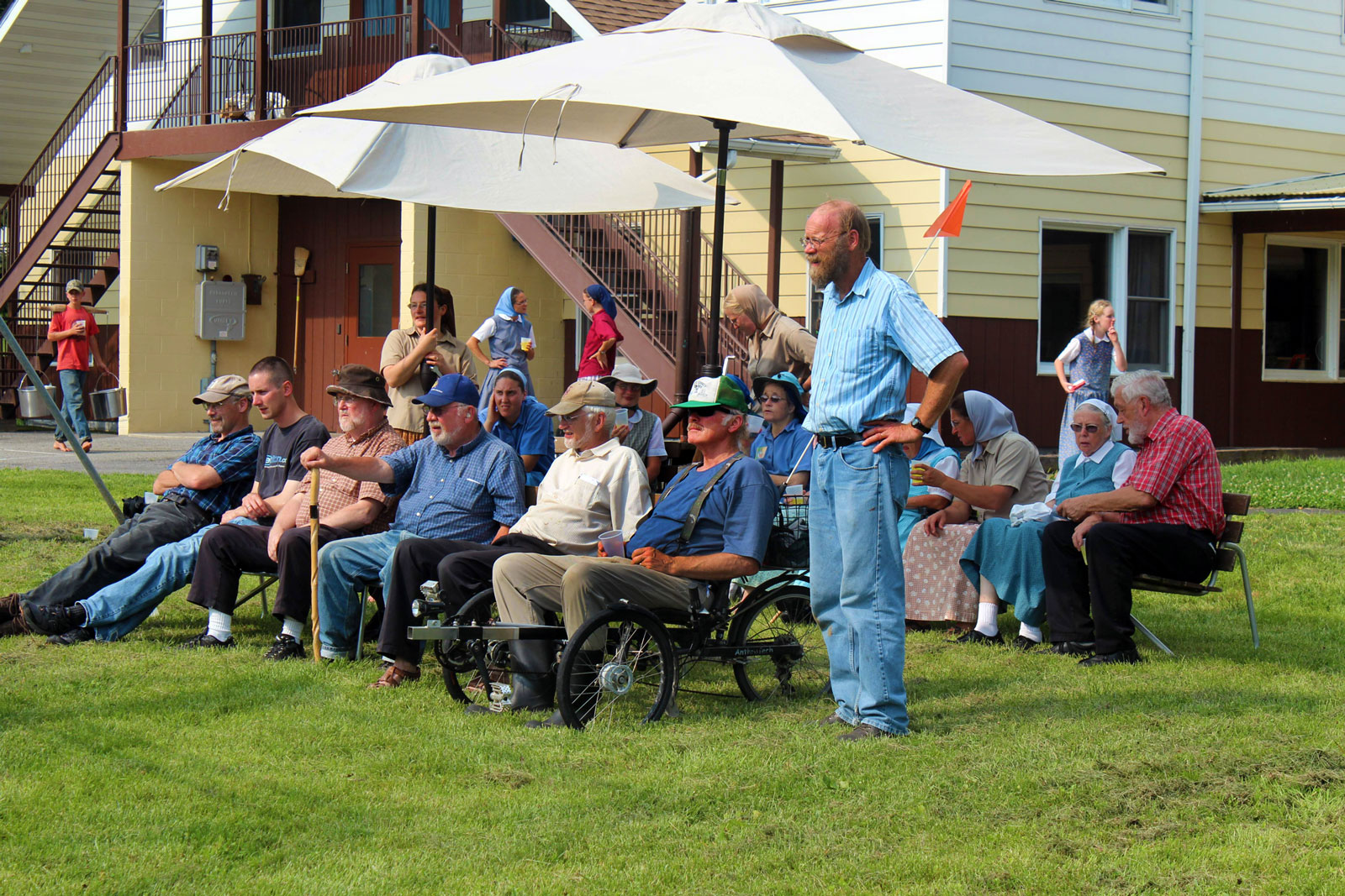 Community gathering outdoors at Maple Ridge Bruderhof with seated attendees under umbrellas.