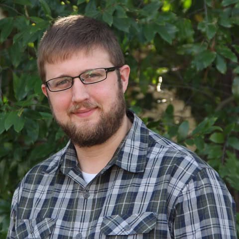 Portrait of a young man with glasses and a plaid shirt outdoors.