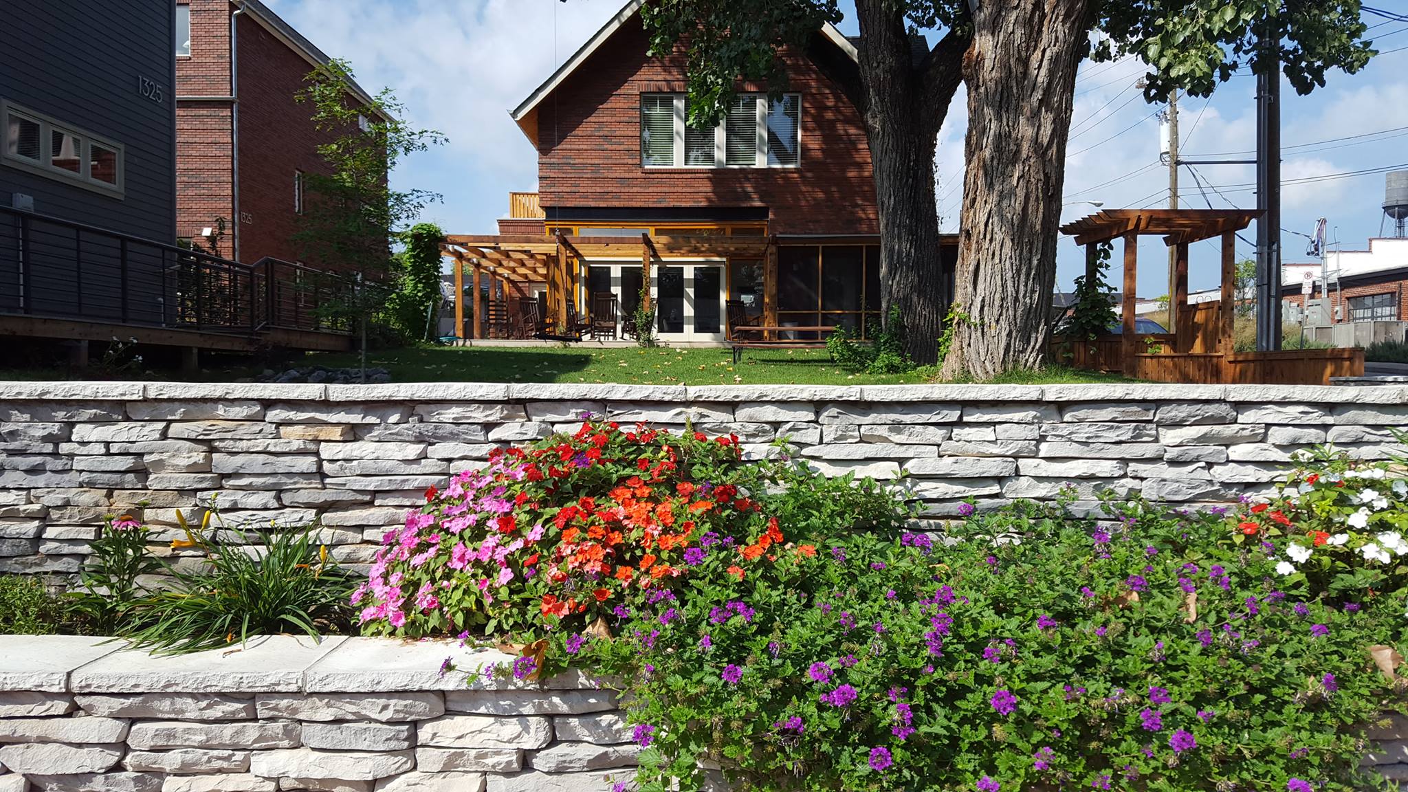 Colorful flower garden with a stone wall and wooden house in the background.