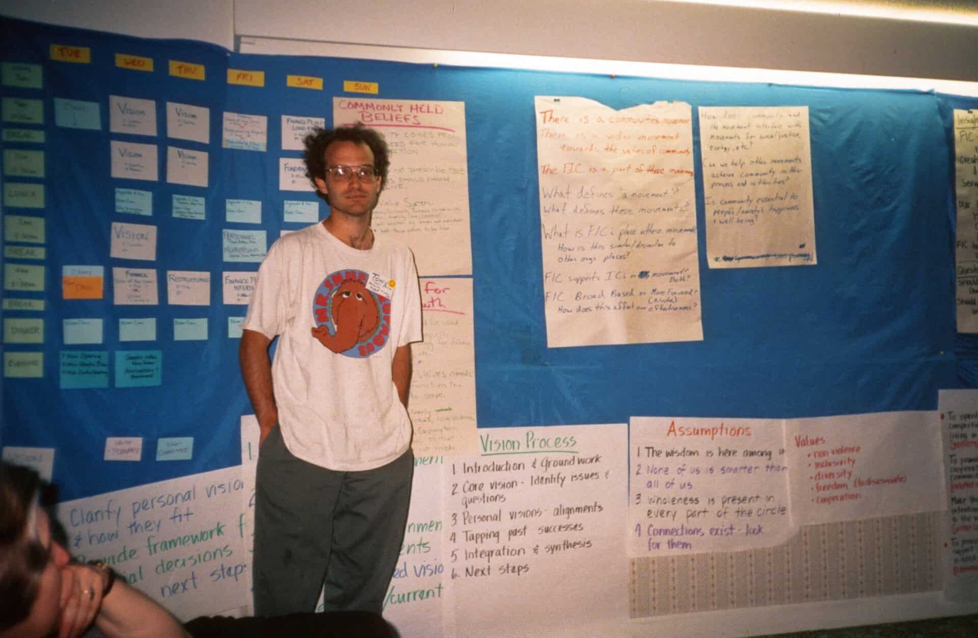 Person standing in front of a blue bulletin board with notes and papers.