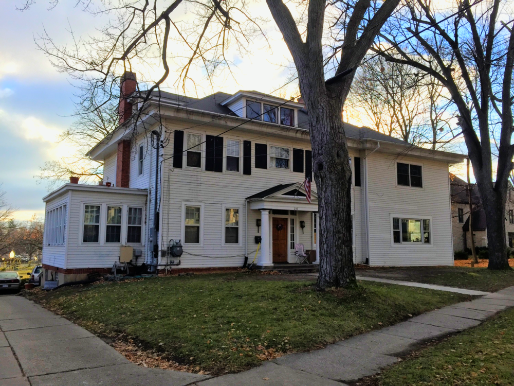 Historic white house with large trees and a well-kept lawn in a neighborhood.