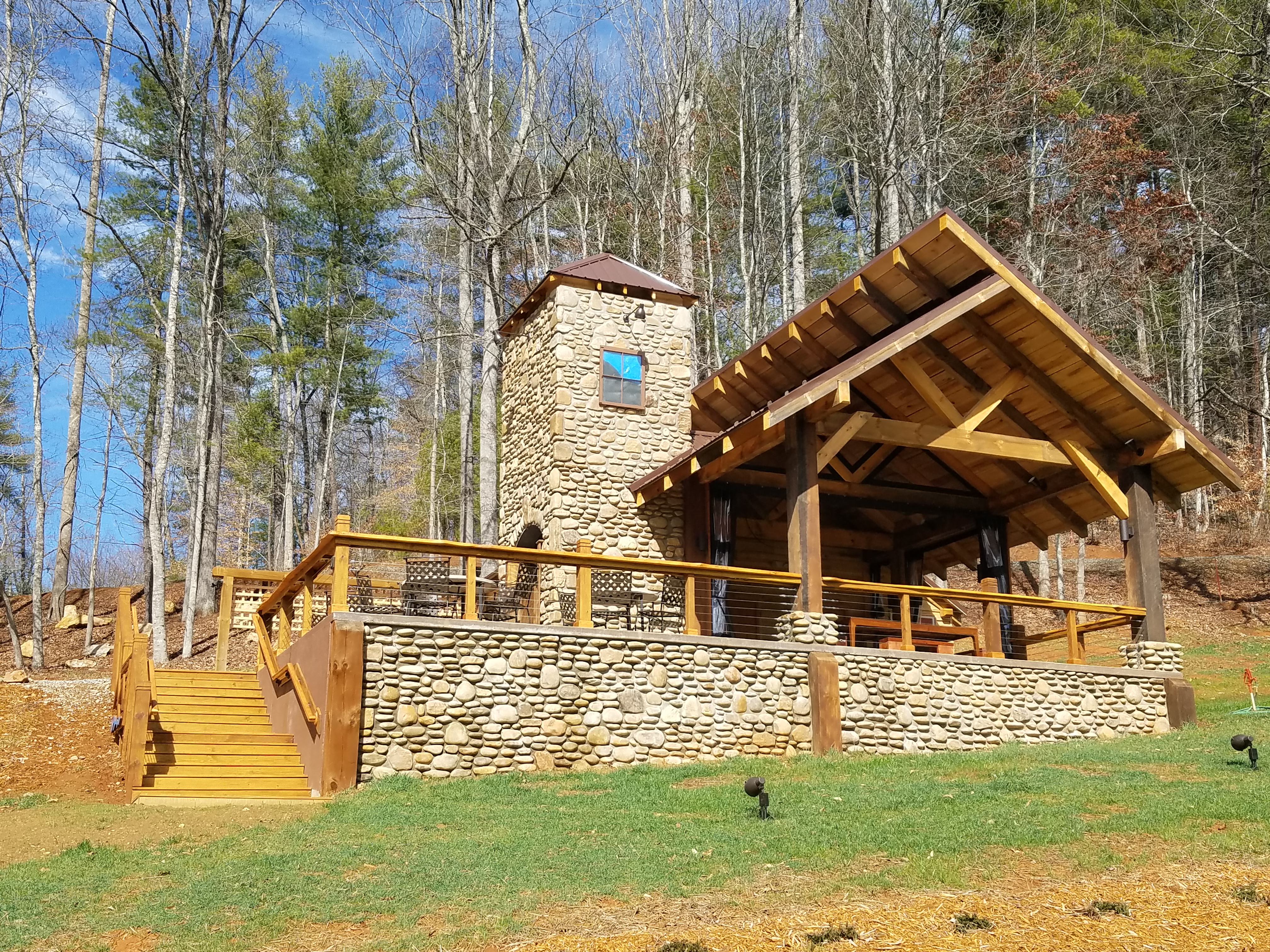 Stone and wood outdoor pavilion with chimney in a wooded area.
