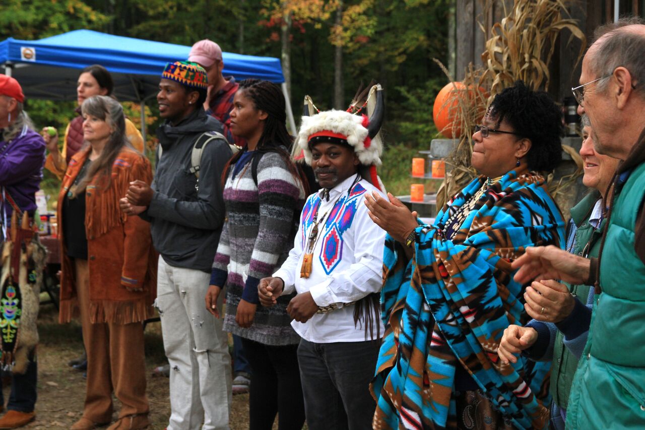 Diverse group of people at outdoor community event with autumn decorations.