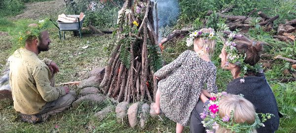 People gathered around a small outdoor fire with a handmade shelter.