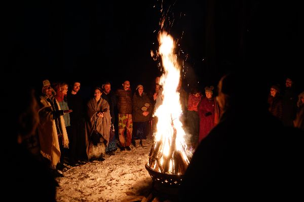 People gathered around a large bonfire at night in a community setting.