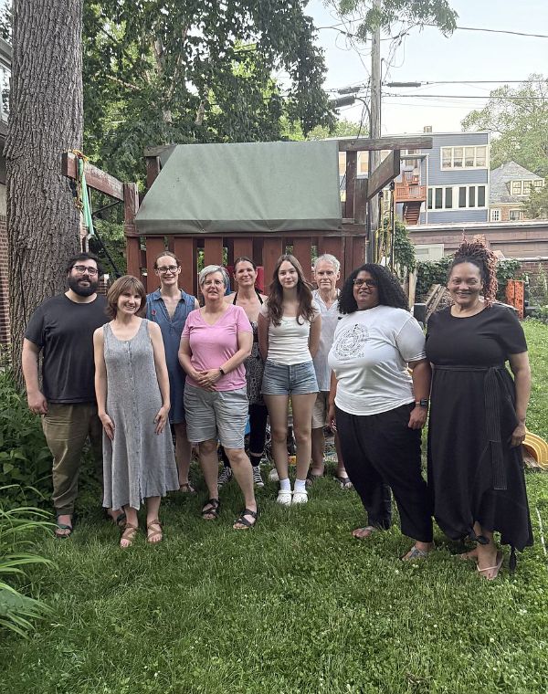 Group of diverse people standing outdoors in front of a wooden playhouse.