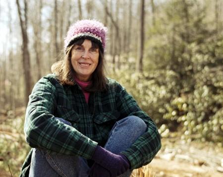 Woman in outdoor forest setting wearing a pink and white knit hat and plaid jacket.