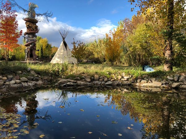 Scenic view of a pond with autumn trees and a tipi in the background.