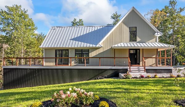 Modern house with metal roof and spacious porch in a green landscape.