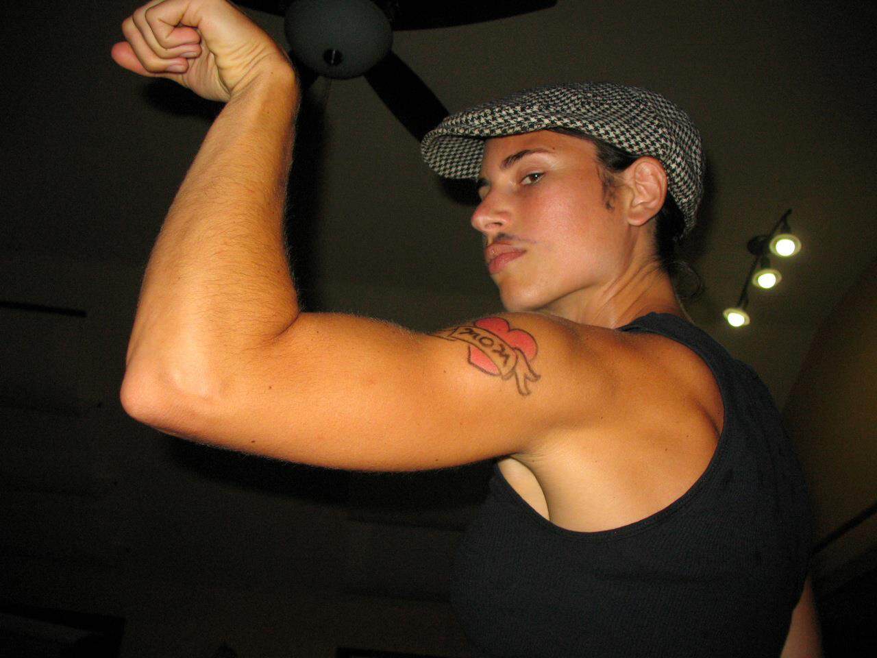 Woman flexing her bicep showing strength and tattoo on arm.
