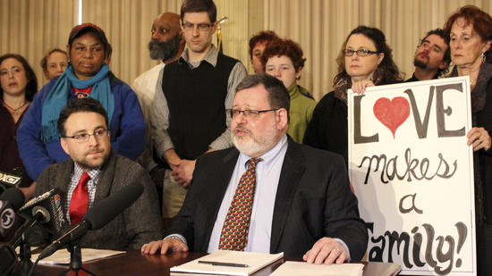 Group of diverse people at a community event with a 'Love makes a family' sign.