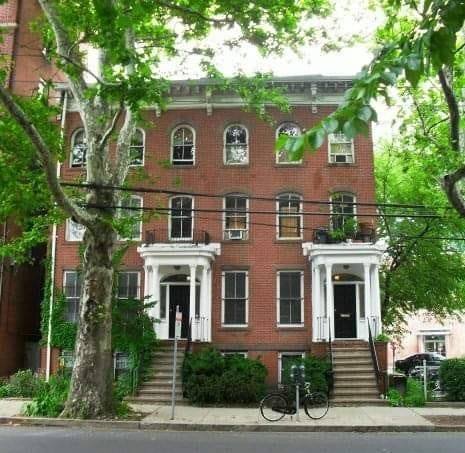 Historic brick row houses in a tree-lined neighborhood with bicycles outside.