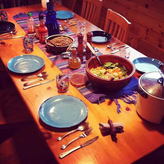Colorful dinner table set with salad, drinks, and utensils in a cozy wooden room.