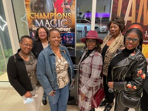 Group of diverse women at a community event in front of a poster.