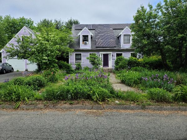 Charming lavender house with lush garden and trees in a residential neighborhood.