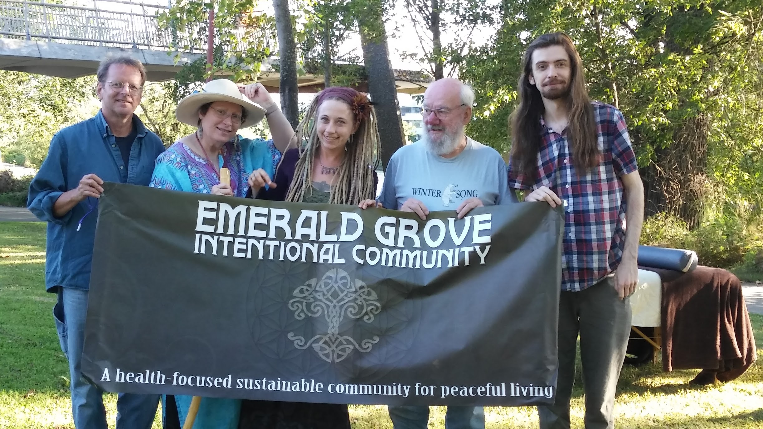 Group of people holding Emerald Grove Intentional Community banner outdoors.