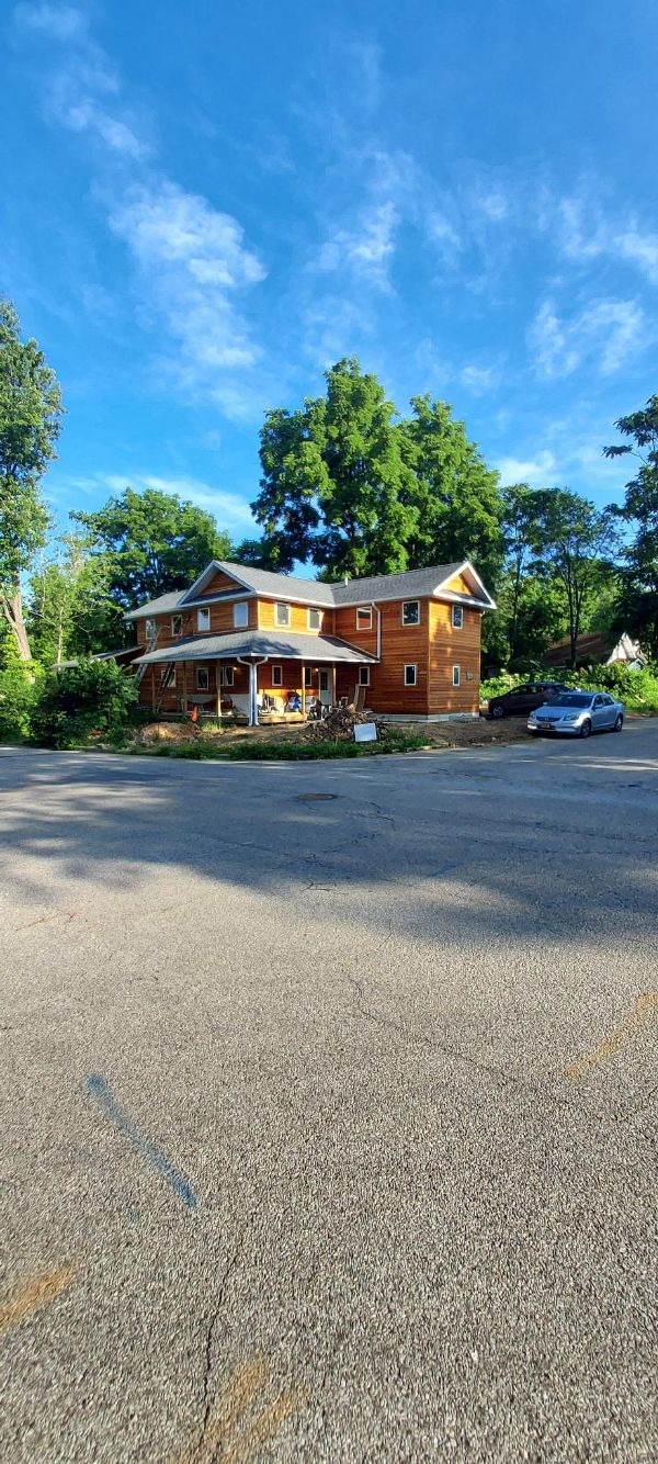 Historic brick building with a porch, surrounded by trees and a parking lot.