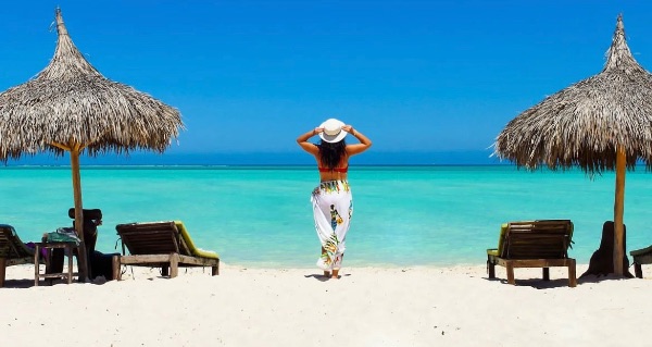 Woman in a hat enjoying a tropical beach with umbrellas and turquoise water.