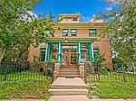 Historic brick building with green accents and lush trees in front.