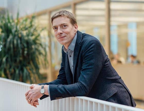 Professional man leaning on a white railing in a modern office space.
