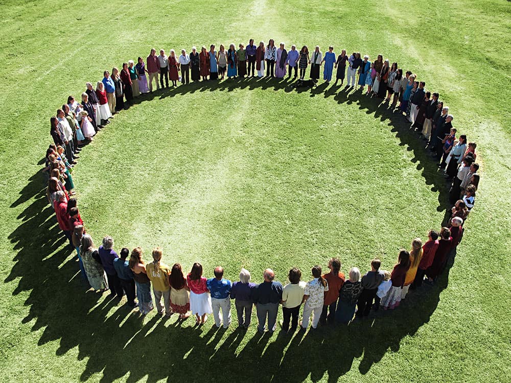 Diverse group of people forming a large circle on green grass.