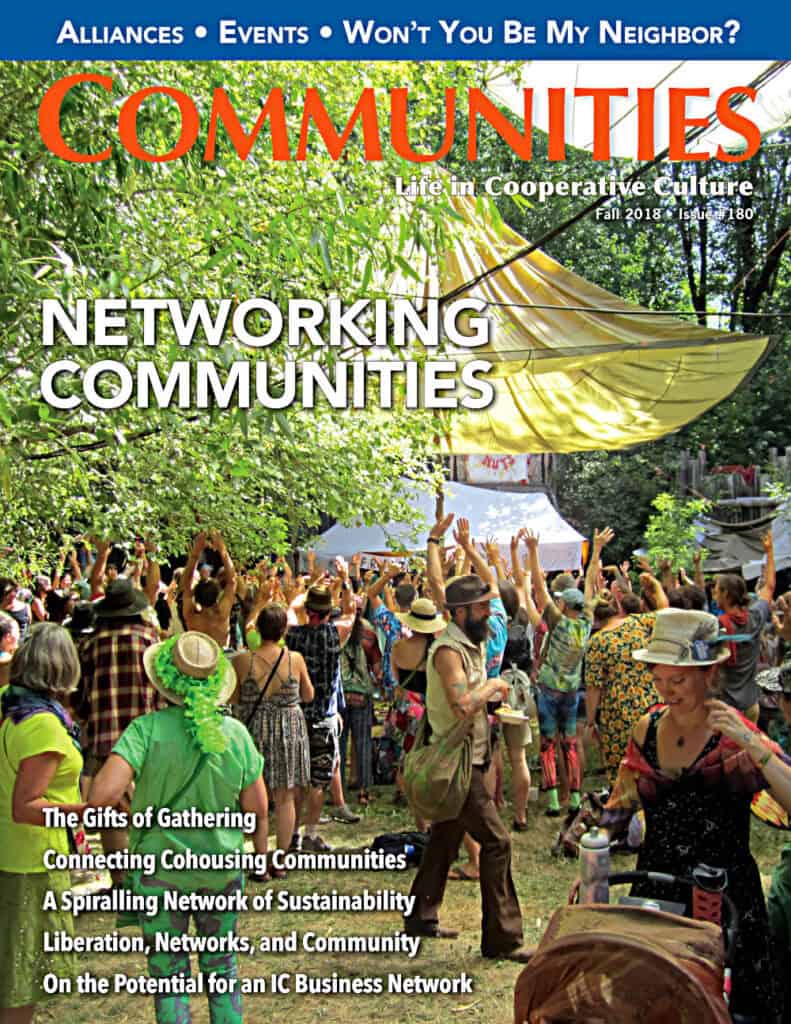 Community gathering at an outdoor event with people raising hands under trees.