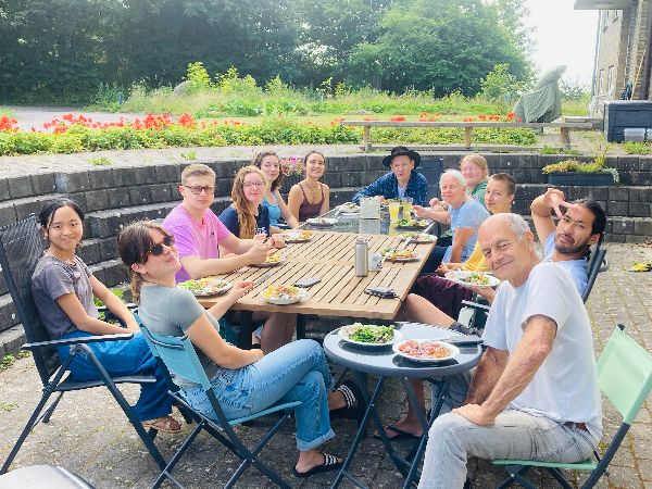 Group of diverse people enjoying outdoor meal at a long table in a garden setting.