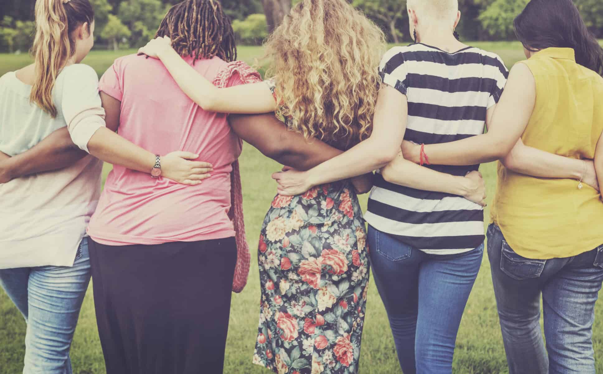 Diverse group of people standing together with arms around each other in a park.