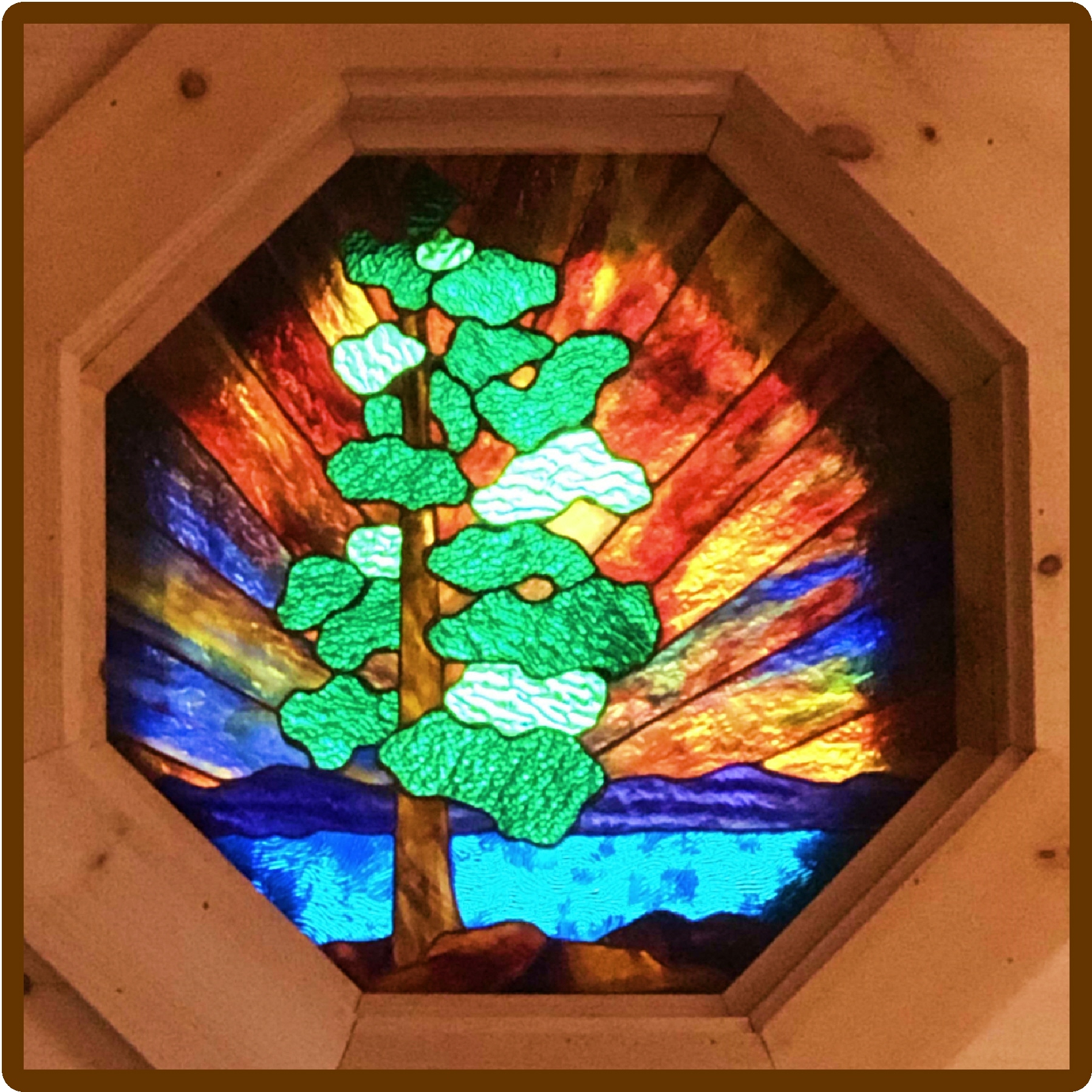 Colorful stained glass window with a tree design and sunset background.