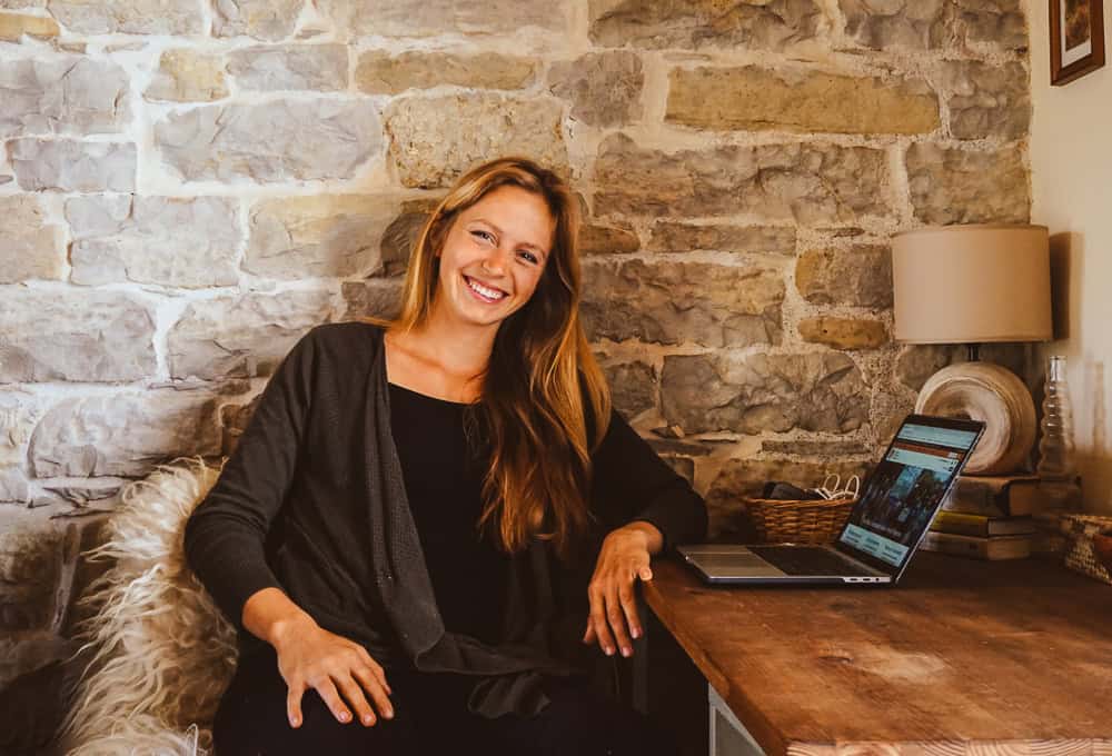 Smiling woman working on laptop at home with stone wall background.