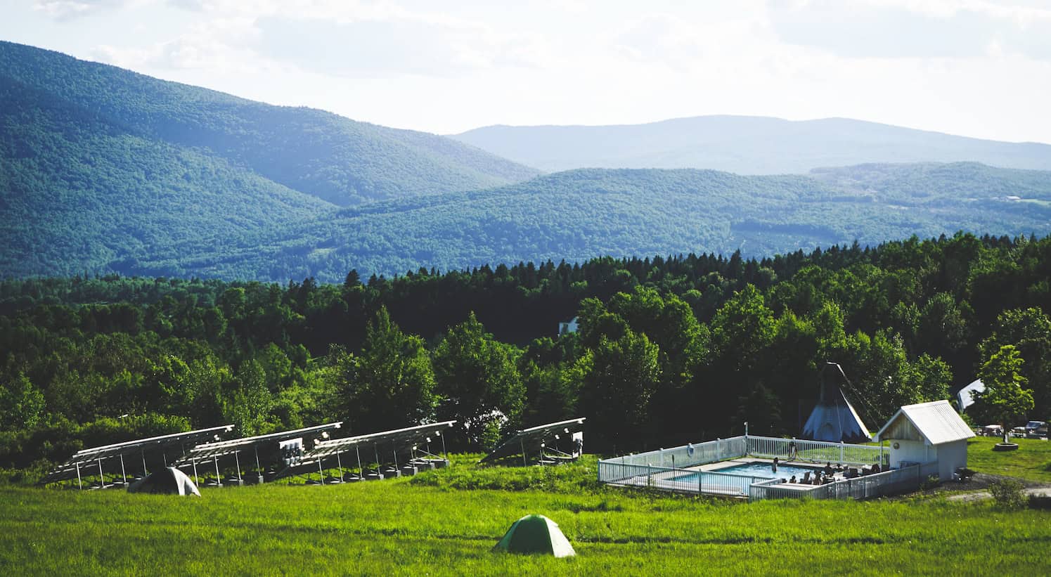 Scenic view of a lush green landscape with mountains and a community farm.