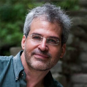 Portrait of a middle-aged man with glasses and gray hair outdoors.