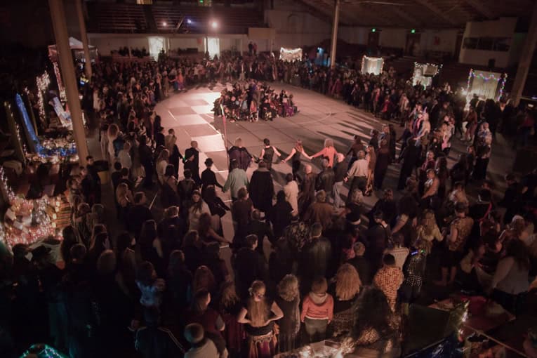 Large indoor gathering with people dancing in a circle at a community event.