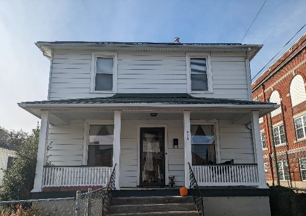 White two-story house with front porch and black door, autumn setting.