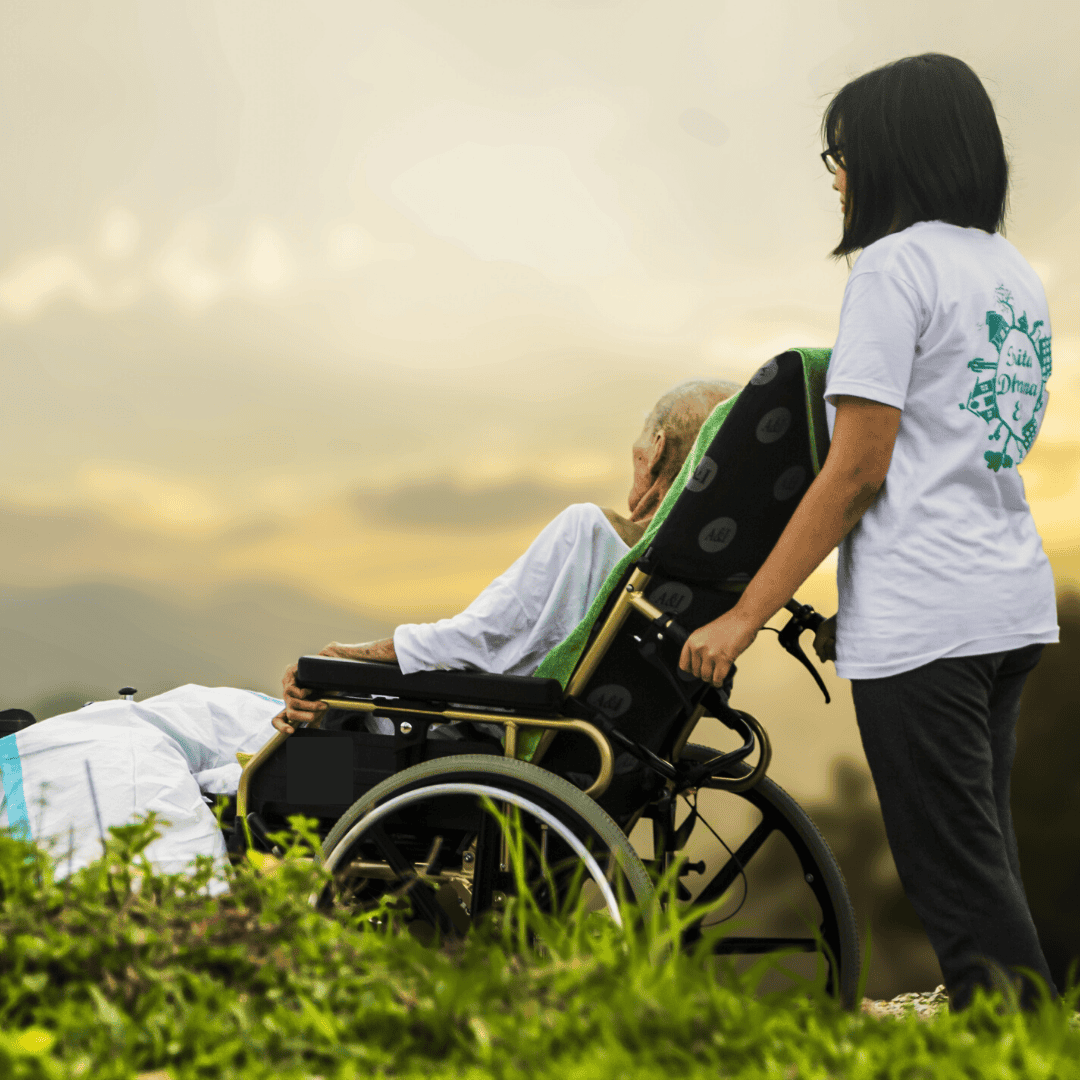 Caregiver pushing elderly person in wheelchair outdoors at sunset.